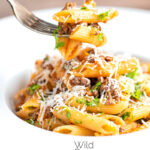 Portrait image of a bolognese style wild boar ragu served with penne pasta being eaten with a text overlay