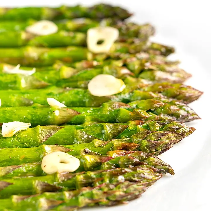 Square image of buttery air fryer cooked asparagus with garlic slices