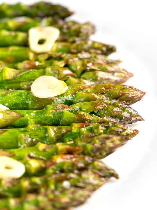 Portrait image of buttery air fryer cooked asparagus with garlic slices