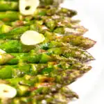 Portrait image of buttery air fryer cooked asparagus with garlic slices and a text overlay