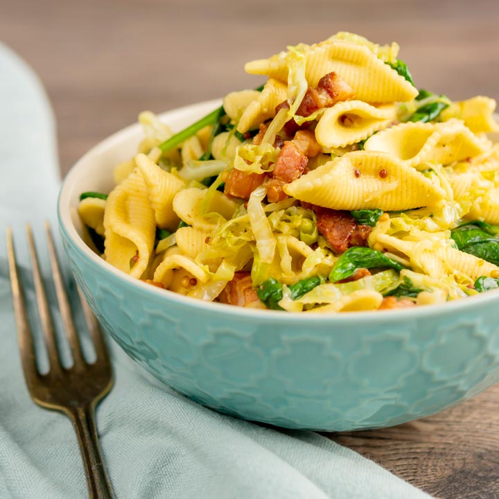 Square image of bacon and savoy cabbage pasta served in a baby blue bowl
