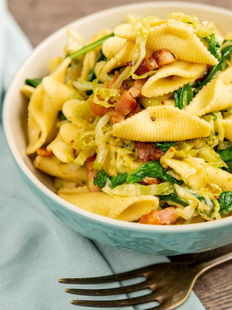 Portrait image of bacon and cabbage pasta served in a baby blue bowl
