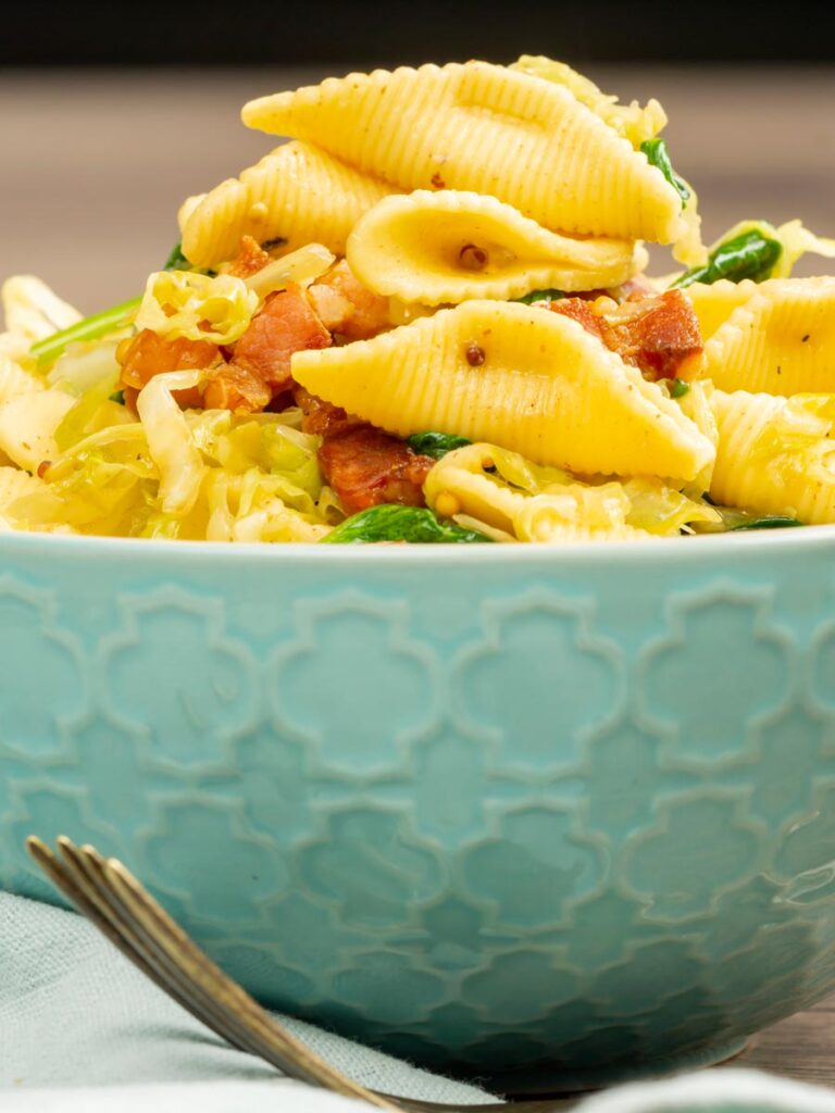 Portrait image of bacon and savoy cabbage pasta served in a baby blue bowl