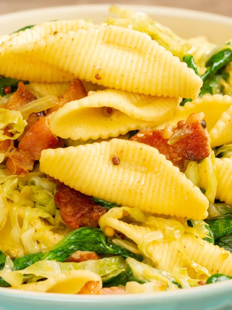 Portrait close up image of bacon and savoy cabbage pasta served in a baby blue bowl