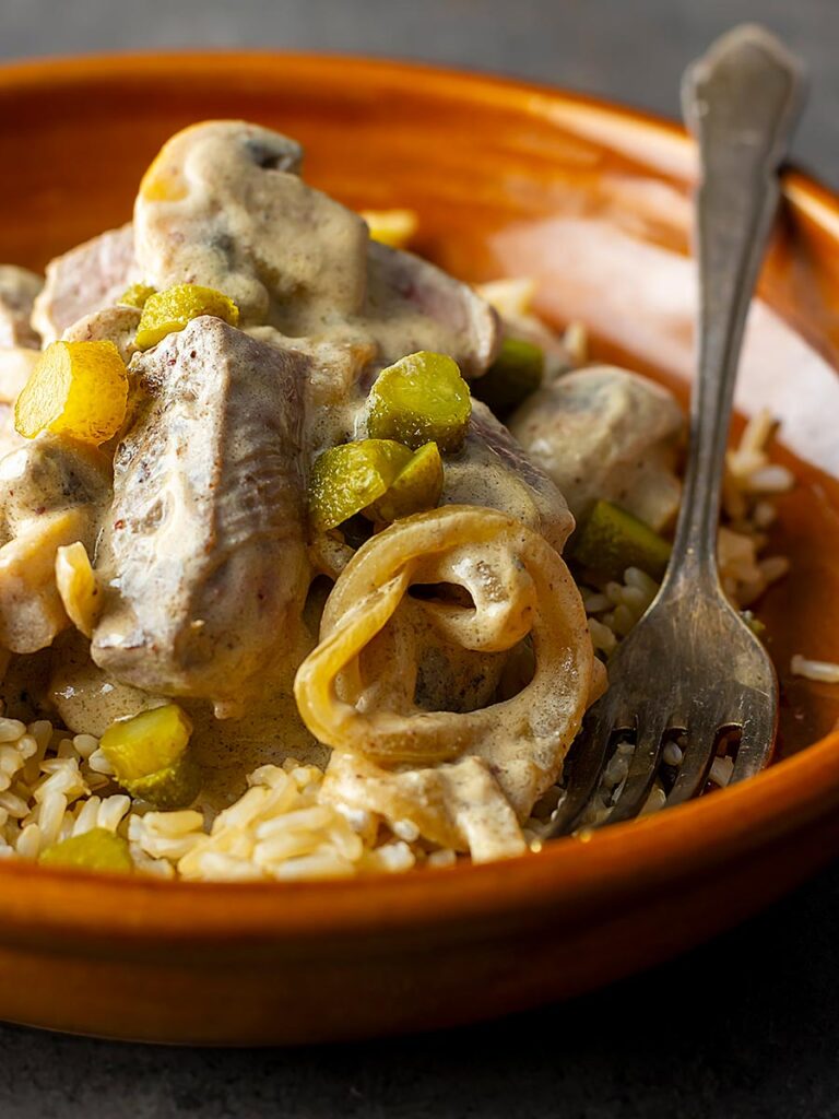 Square close up image of a beef stroganoff with mushrooms served in an earthenware bowl