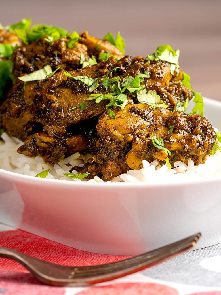 Portrait close up image of a dry pepper chicken Chettinad curry served on boiled basmati rice.