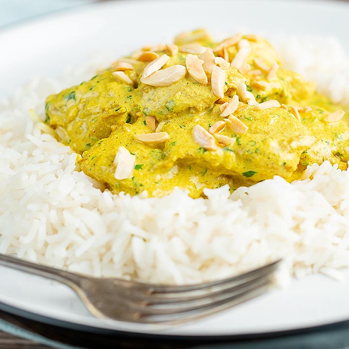 Square image of a creamy chicken korma curry served with boiled rice and toasted almonds.