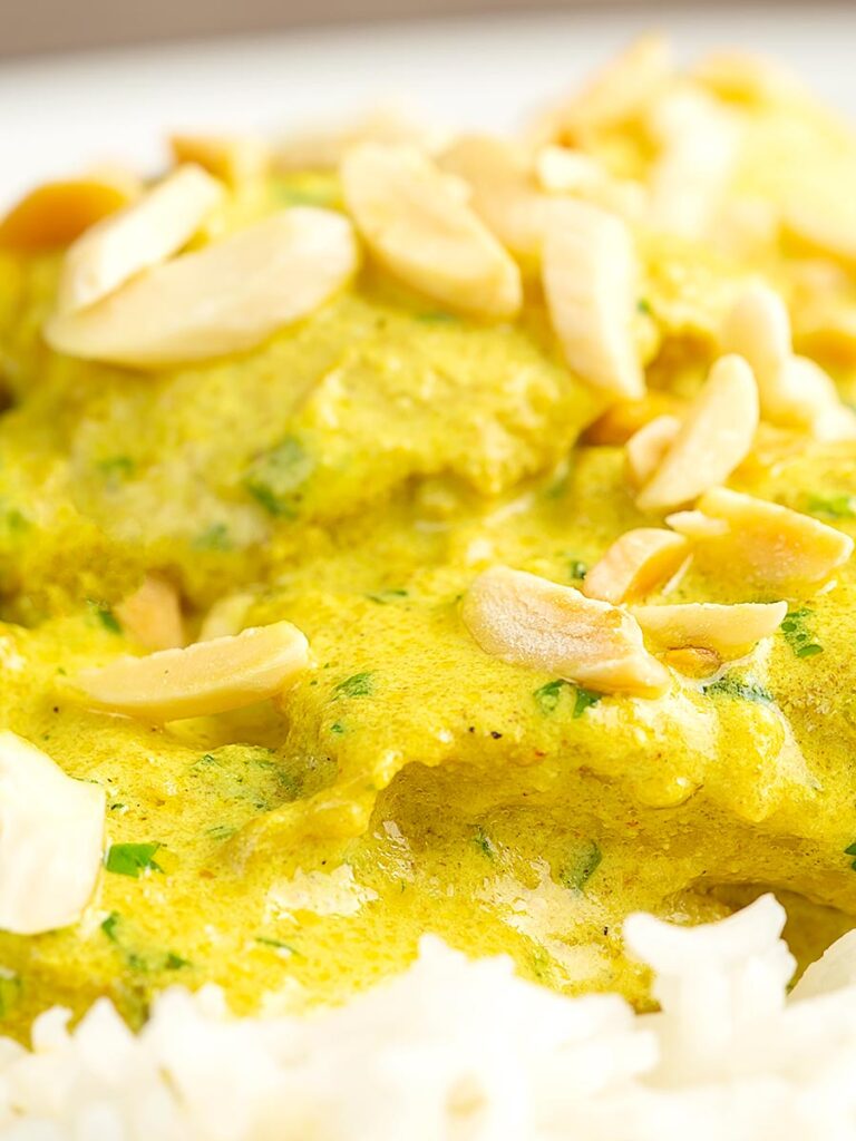 Portrait close up image of a creamy chicken korma curry served with boiled rice and toasted almonds.