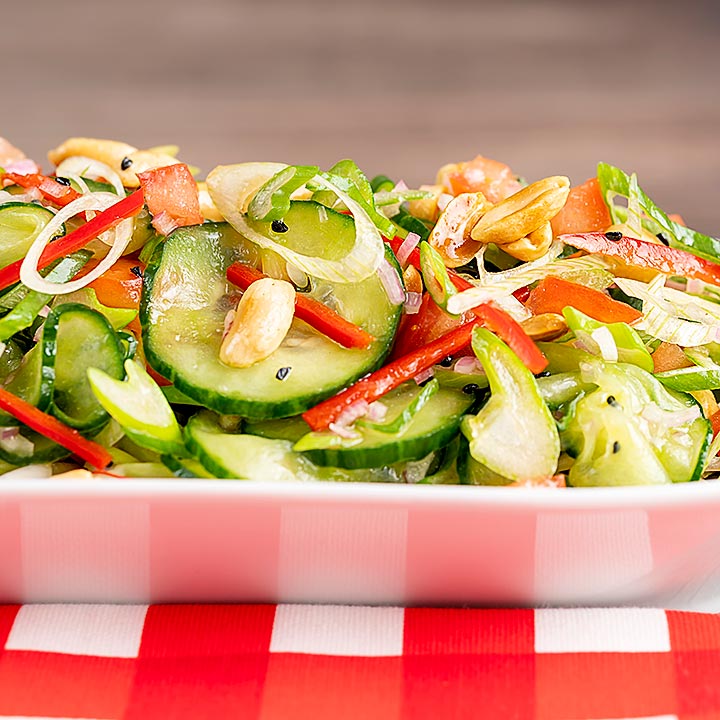 Square image of a vibrant cucumber salad featuring chilli, tomatoes, spring onion and toasted peanuts