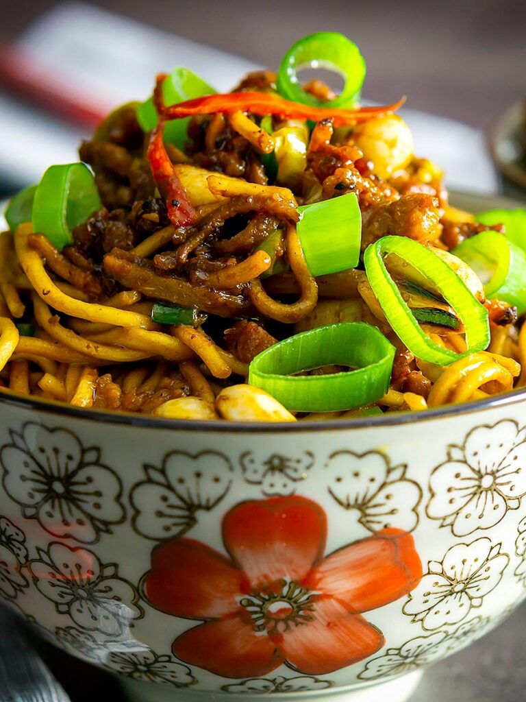 Portrait close up image of Dan Dan Noodles served in an Asian style bowl decorated with a red flower