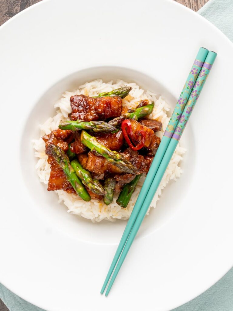 Portrait overhead image of Korean Pork Belly cooked in a spicy coating with asparagus
