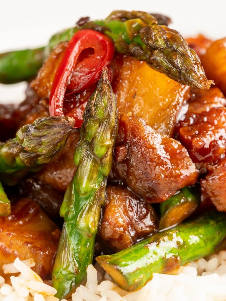 Portrait close up image of Korean Pork Belly cooked in a spicy coating with asparagus