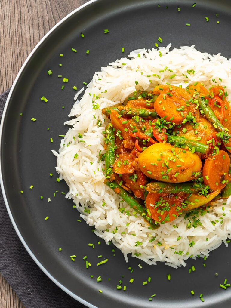 Portrait overhead image of a mixed vegetable karahi curry served on a bed of boiled rice with snipped chives