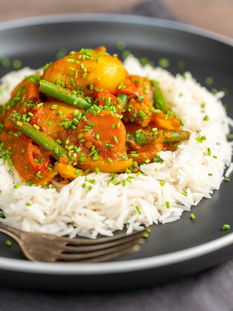 Portrait image of a mixed vegetable karahi curry served on a bed of boiled rice with snipped chives
