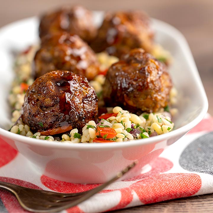 Square image of Moroccan influenced meatballs with a pomegranate molasses glaze served on a tabbouleh salad