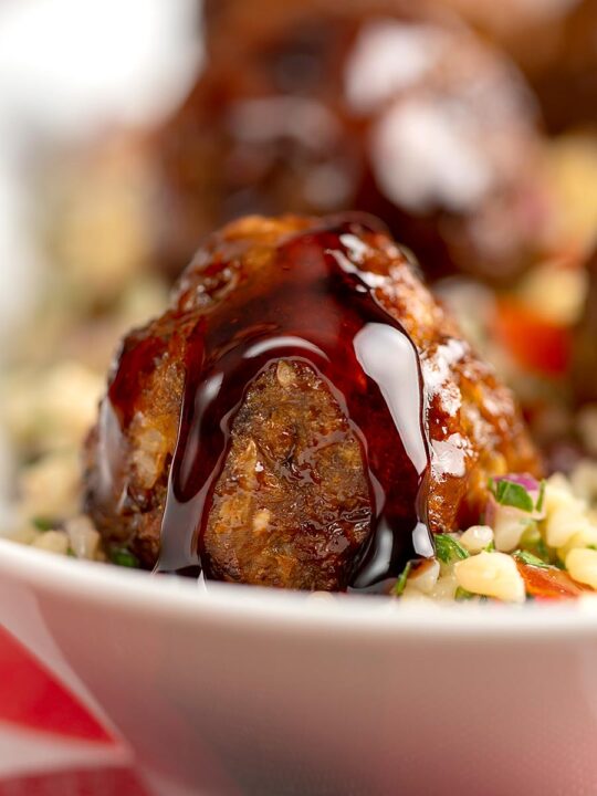 Portrait close up image of North African influenced meatballs with a pomegranate molasses glaze served on a tabbouleh salad