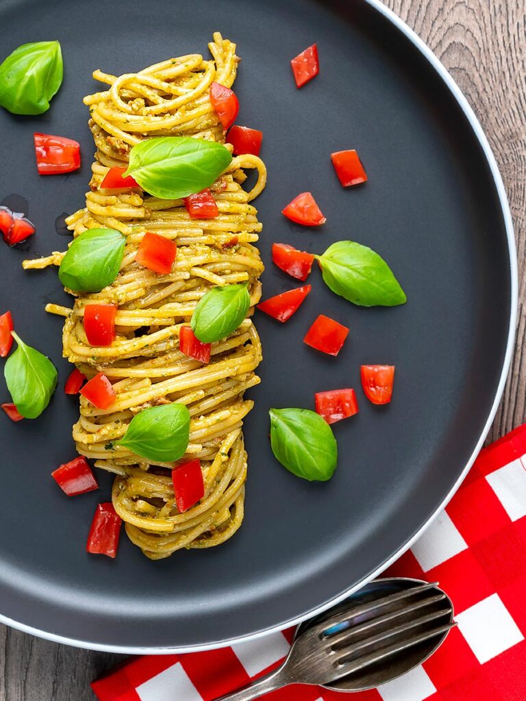 Portrait overhead image of pesto alla trapanese served with spaghetti and tomato concasse and fresh basil