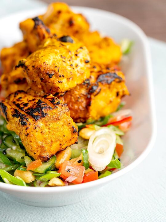 Portrait image of grilled salmon tikka served on a cucumber salad