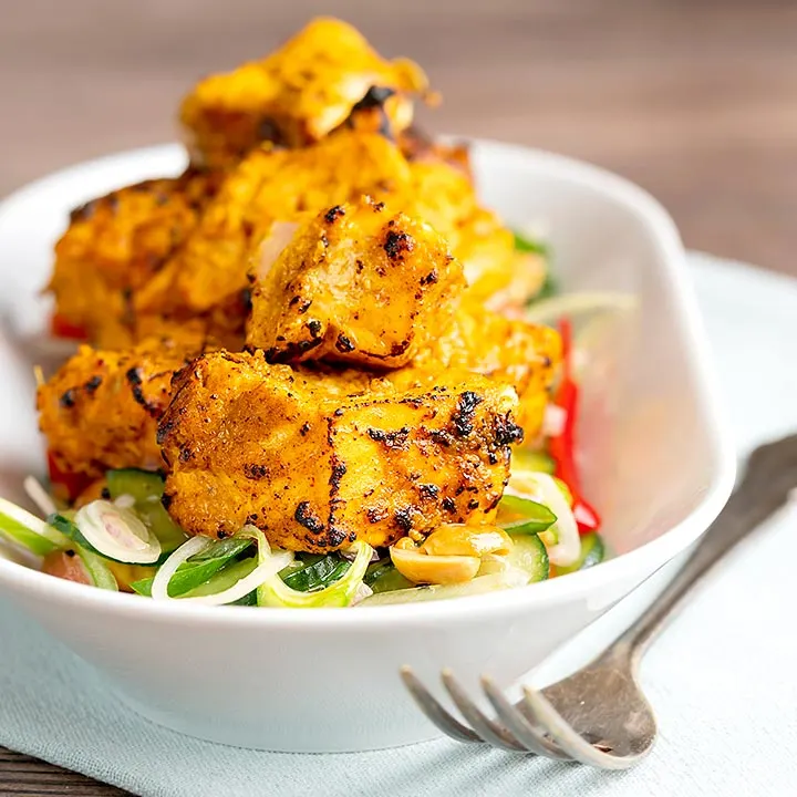 Square image of grilled salmon tikka served on a cucumber salad