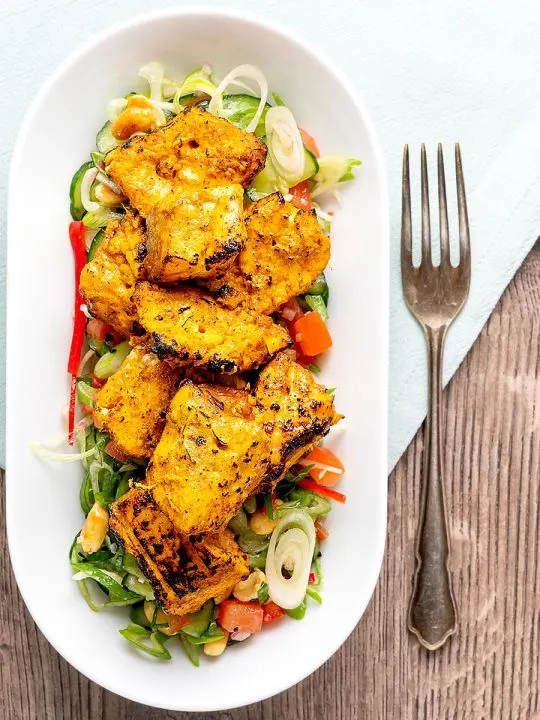 Portrait overhead image of grilled salmon tikka served on a cucumber salad