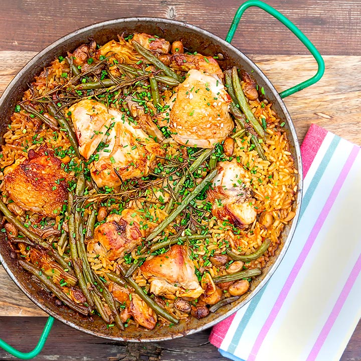 square overhead image of a traditional Valencian paella featuring rabbit and chicken served in a paella pan