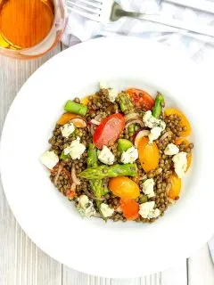 Square overhead image of an asparagus salad with lentils, blue cheese and tomatoes served in a white bowl