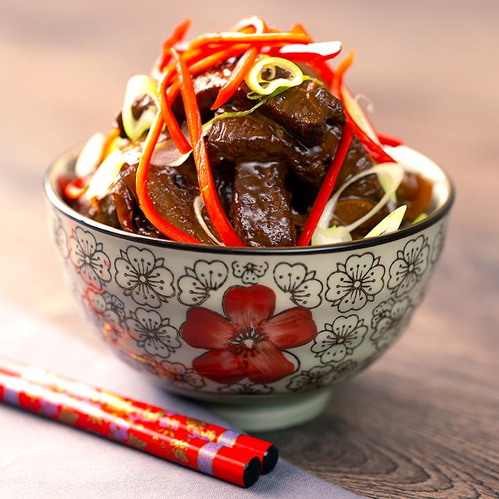 Beef in oyster sauce stir fry served in a bowl decorated with an Asian flower design garnished with chilli and spring onion.