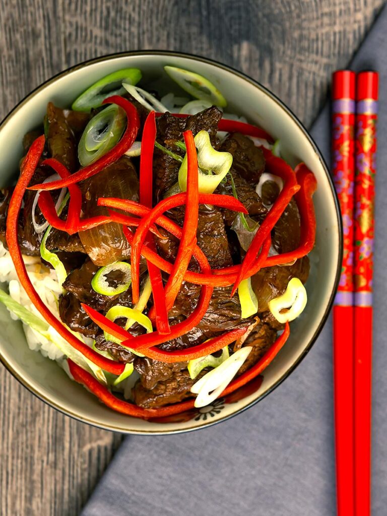 Portrait overhead image of Beef in oyster sauce stir fry served in a bowl garnished with chilli and spring onion