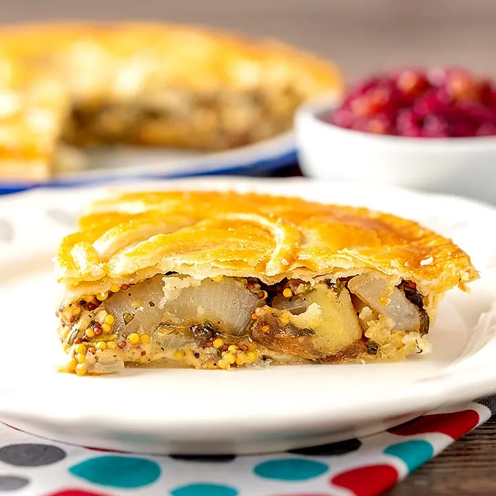 Square image of a slice of cheese and onion pie with wholegrain mustard