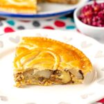 Portrait image of a slice of cheese and onion pie with wholegrain mustard with the whole pie in the background