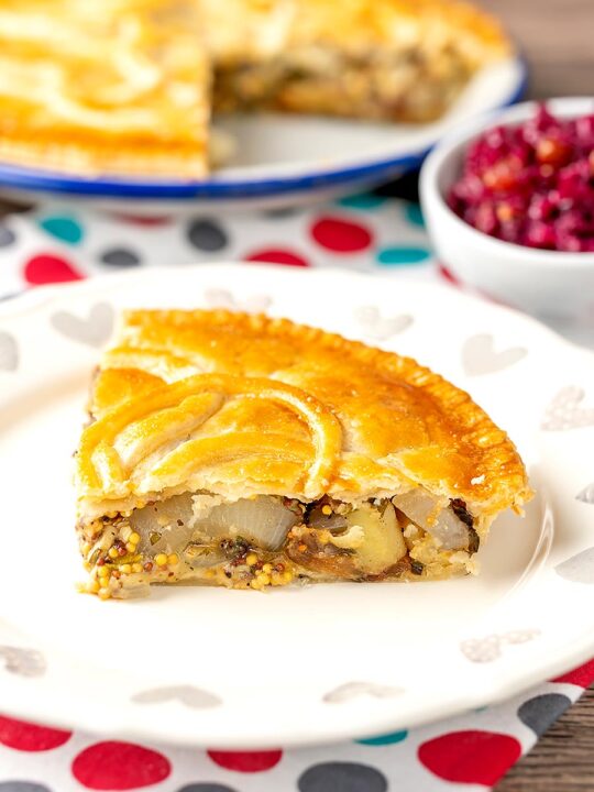 Portrait image of a slice of cheese and onion pie with wholegrain mustard with the whole pie in the background