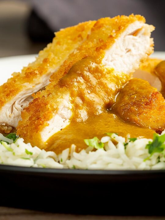 Portrait close up image of a chicken katsu curry with sliced crispy chicken breast served with coriander rice