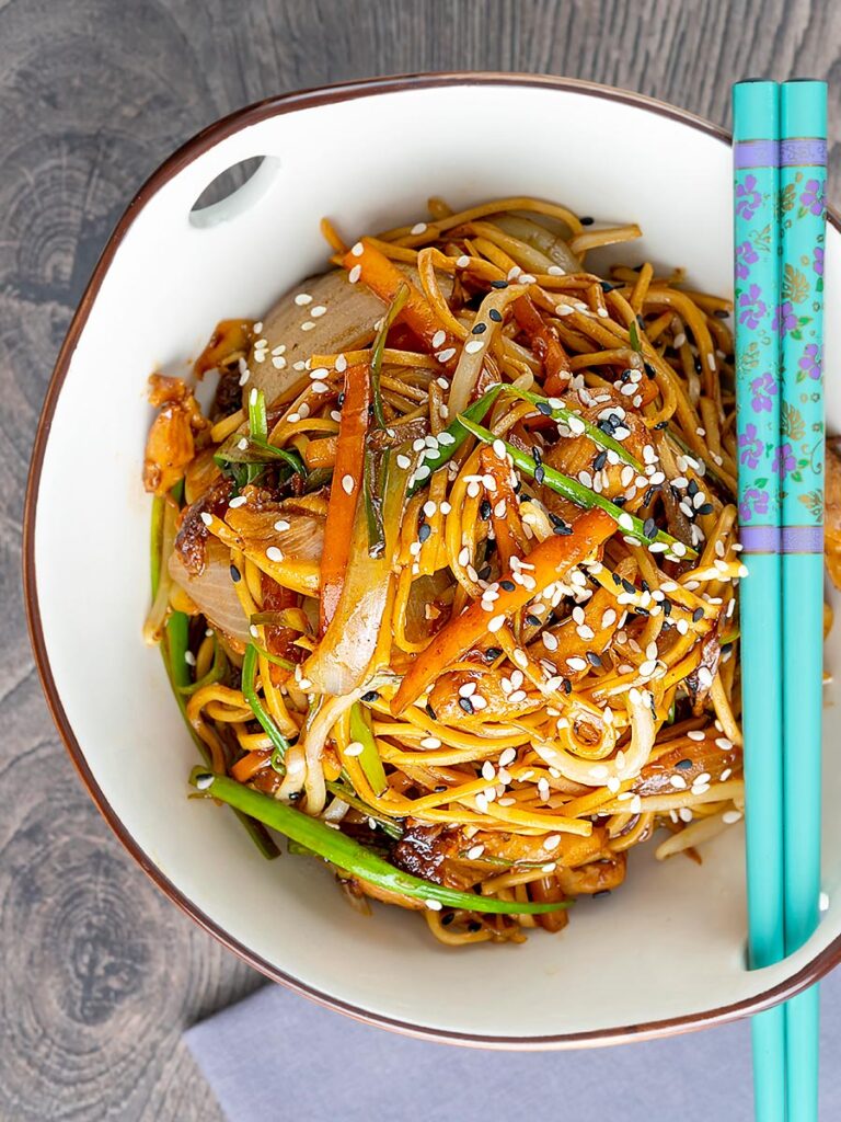 Portrait close up imag of a chicken noodle stir fry, lo mein or chow mein with turquoise chop sticks