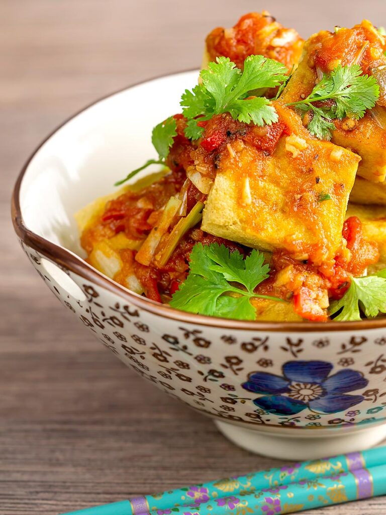 Portrait image of crispy cubes fried tofu with a Vietnamese tomato sauce and coriander leaves in an bowl
