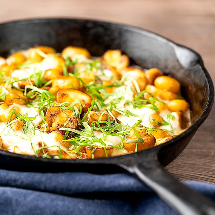 Square image of baked gnocchi with mushrooms in balsamic vinegar, mozzarella cheese and fresh basil served in a cast iron skillet