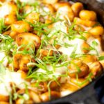 Portrait image of baked gnocchi with mushrooms in balsamic vinegar, mozzarella cheese and fresh basil served in a cast iron skillet