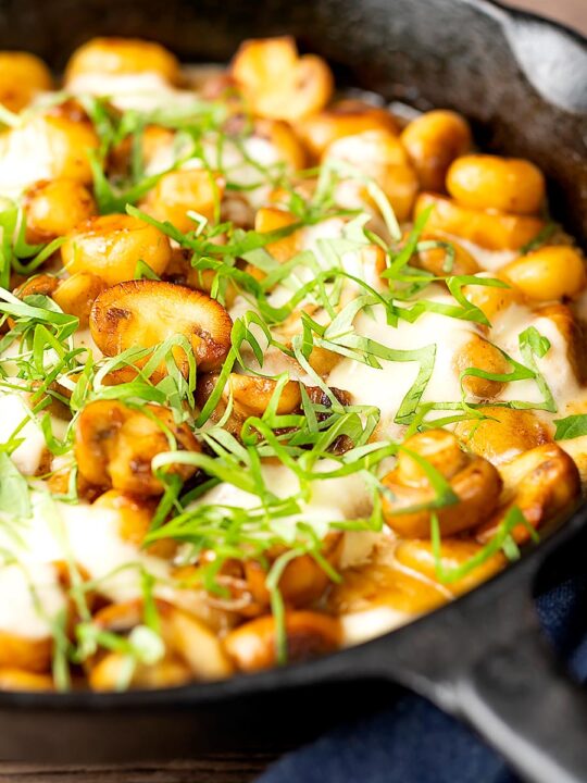 Portrait image of baked gnocchi with mushrooms in balsamic vinegar, mozzarella cheese and fresh basil served in a cast iron skillet