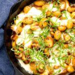 Portrait overhead image of baked gnocchi with mushrooms in balsamic vinegar, mozzarella cheese and fresh basil served in a cast iron skillet