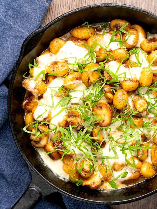 Portrait overhead image of baked gnocchi with mushrooms in balsamic vinegar, mozzarella cheese and fresh basil served in a cast iron skillet