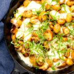 Portrait overhead image of baked gnocchi with mushrooms in balsamic vinegar, mozzarella cheese and fresh basil served in a cast iron skillet with text overlay