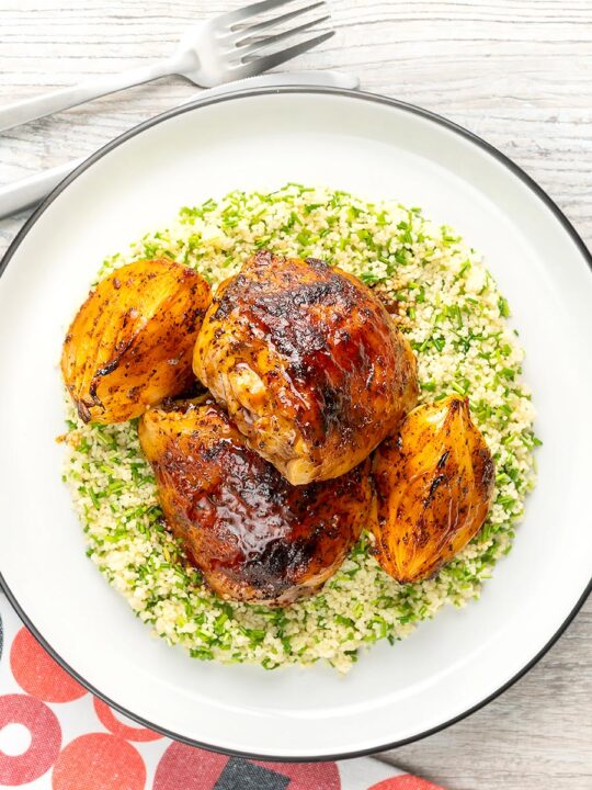 Portrait overhead image of roasted harissa chicken thighs with onion wedges served on herbed couscous