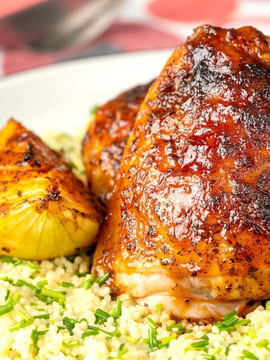 Portrait close up image of roasted harissa chicken thighs with onion wedges served on herbed couscous