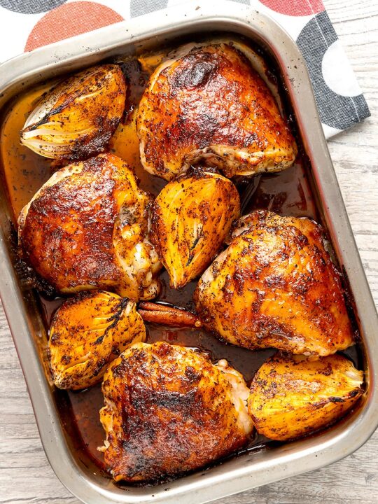 Portrait overhead image of roasted harissa chicken thighs with onion wedges in a roasting tin