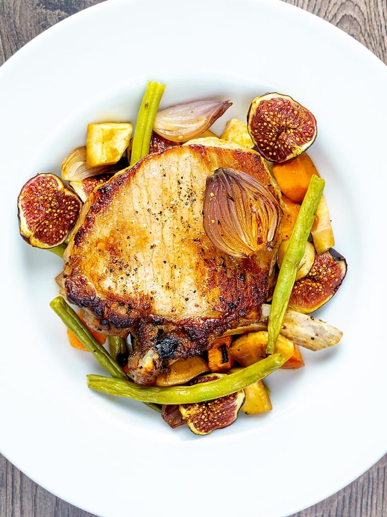 Portrait overhead image Pork chops with figs form a tray bake served in a shallow white bowl