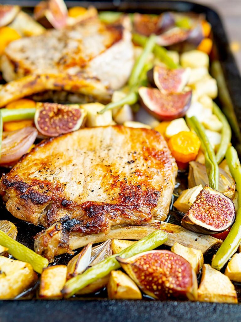 Portrait image of a pork chop tray bake with figs, green beans and roots