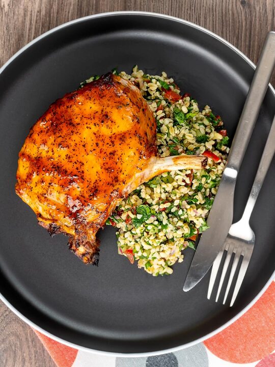 Portrait overhead image of harissa glazed roast pork chops served on a grey plate with tabbouleh salad