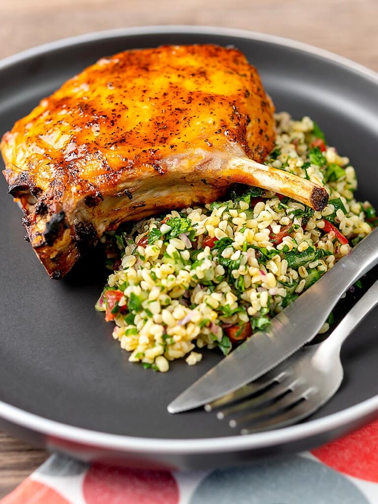 Portrait image of harissa glazed roast pork chops served on a grey plate with tabbouleh salad