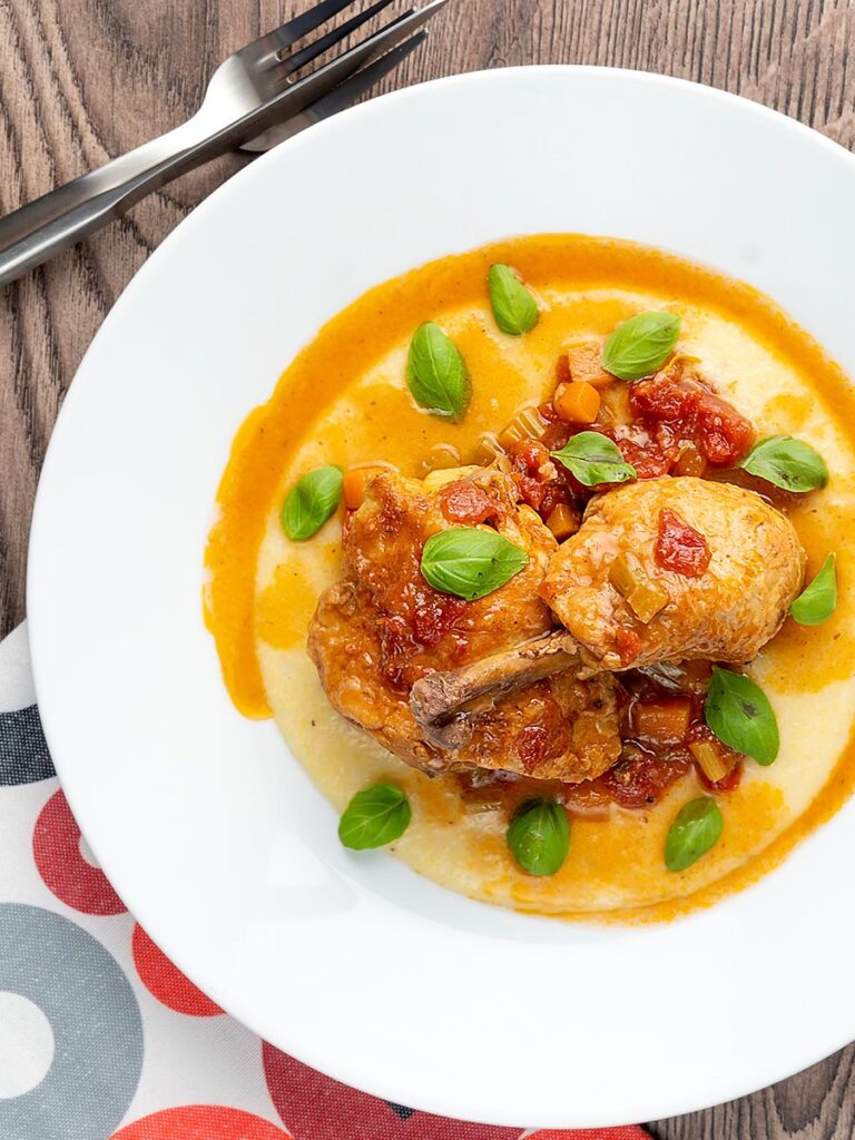 Portrait overhead image of slow cooker chicken cacciatore served on a bed of polenta