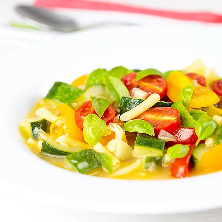 Square image of a summer vegetable soup featuring courgettes, tomato and new potatoes served in a white bowl