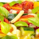 Portrait close up image of a summer vegetable soup featuring courgettes, tomato and new potatoes